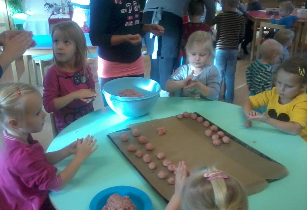 Lapsia ja aikuisia pöydän ääressä, valmistamassa yhdessä lihapullia