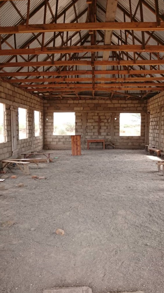 Kirkon rakennustyömaalta Tansaniasta. Kuva sisältä, jossa näkyvät kattotuolit. Kirkossa maalattia, ikkunat puuttuvat sekä penkit..