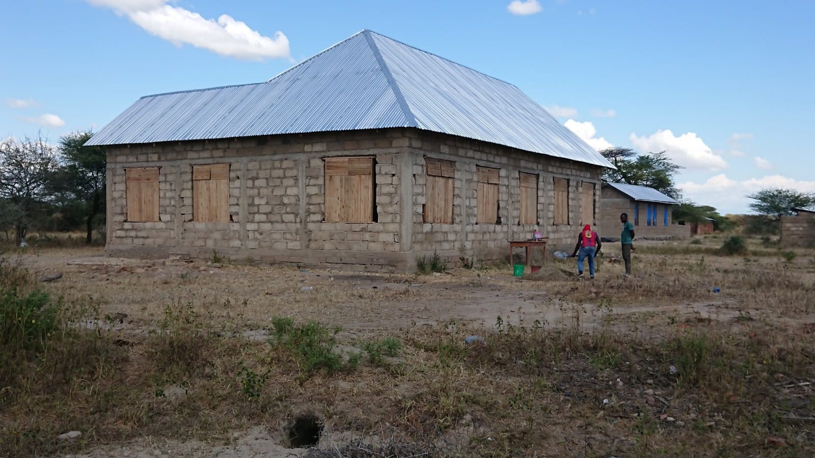 Kirkon rakennustyömaalta Tansaniasta. Tiilistä tehdyssä seinässä ikkuna-aukot ikkunat peitetty laudoista tehdyillä luukuilla.